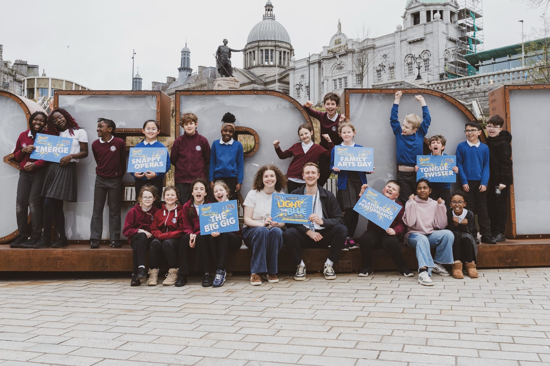 Cheerful group of children holding event signs, posing happily in Aberdeen city centre.