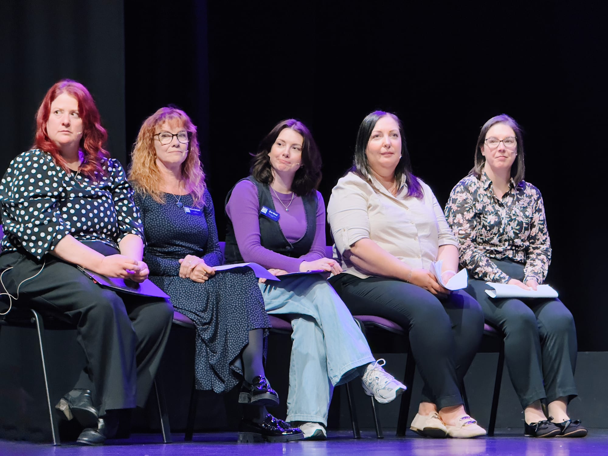 Five women sit on stage holding papers, likely part of a discussion or presentation at the Arts Centre.