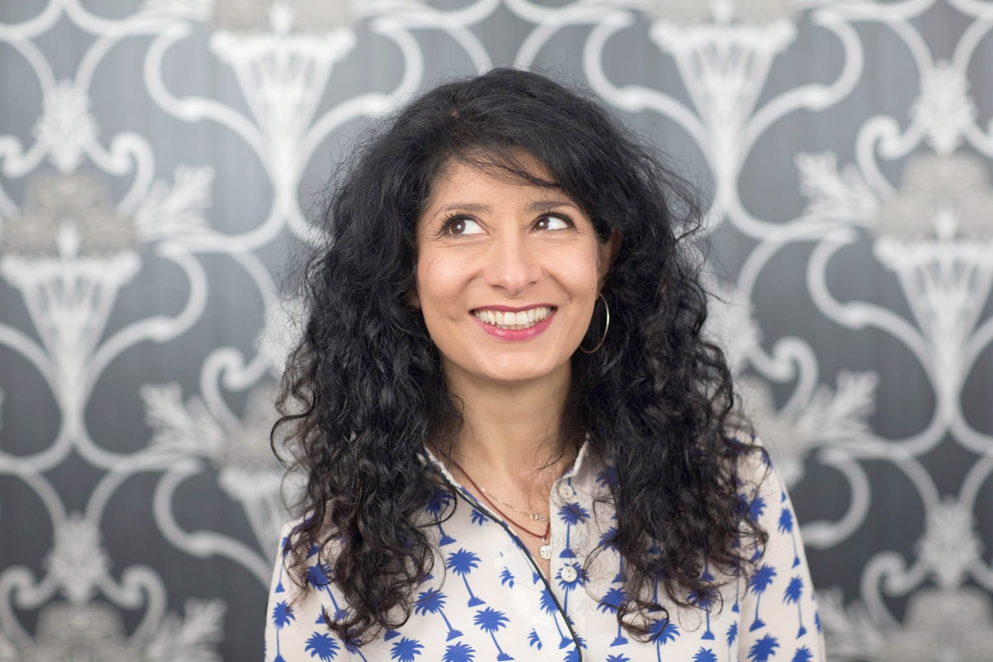 Shaparak Khorsandi smiling, curly dark hair, patterned blouse