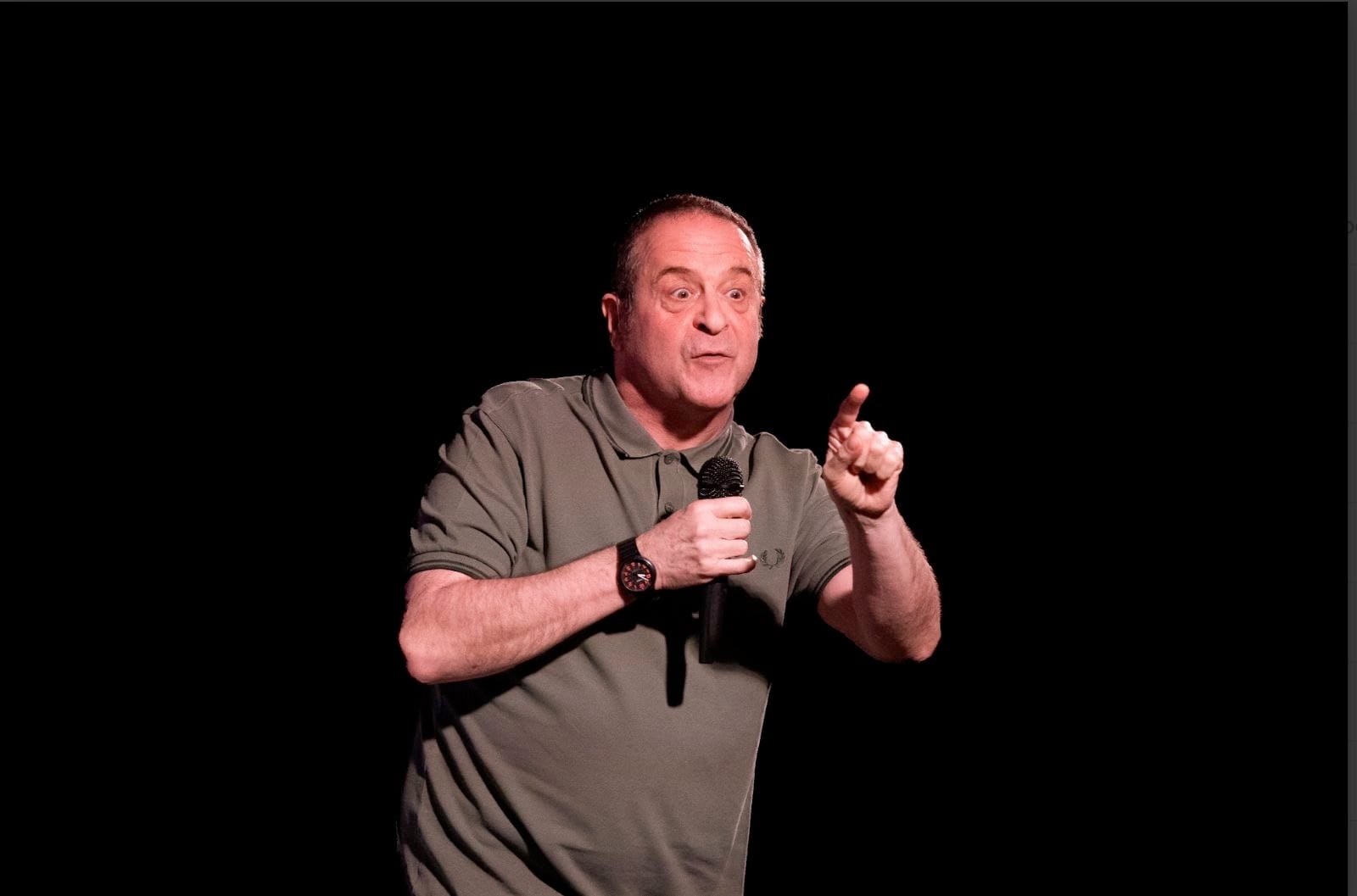 Mark Thomas performing on stage, microphone in hand