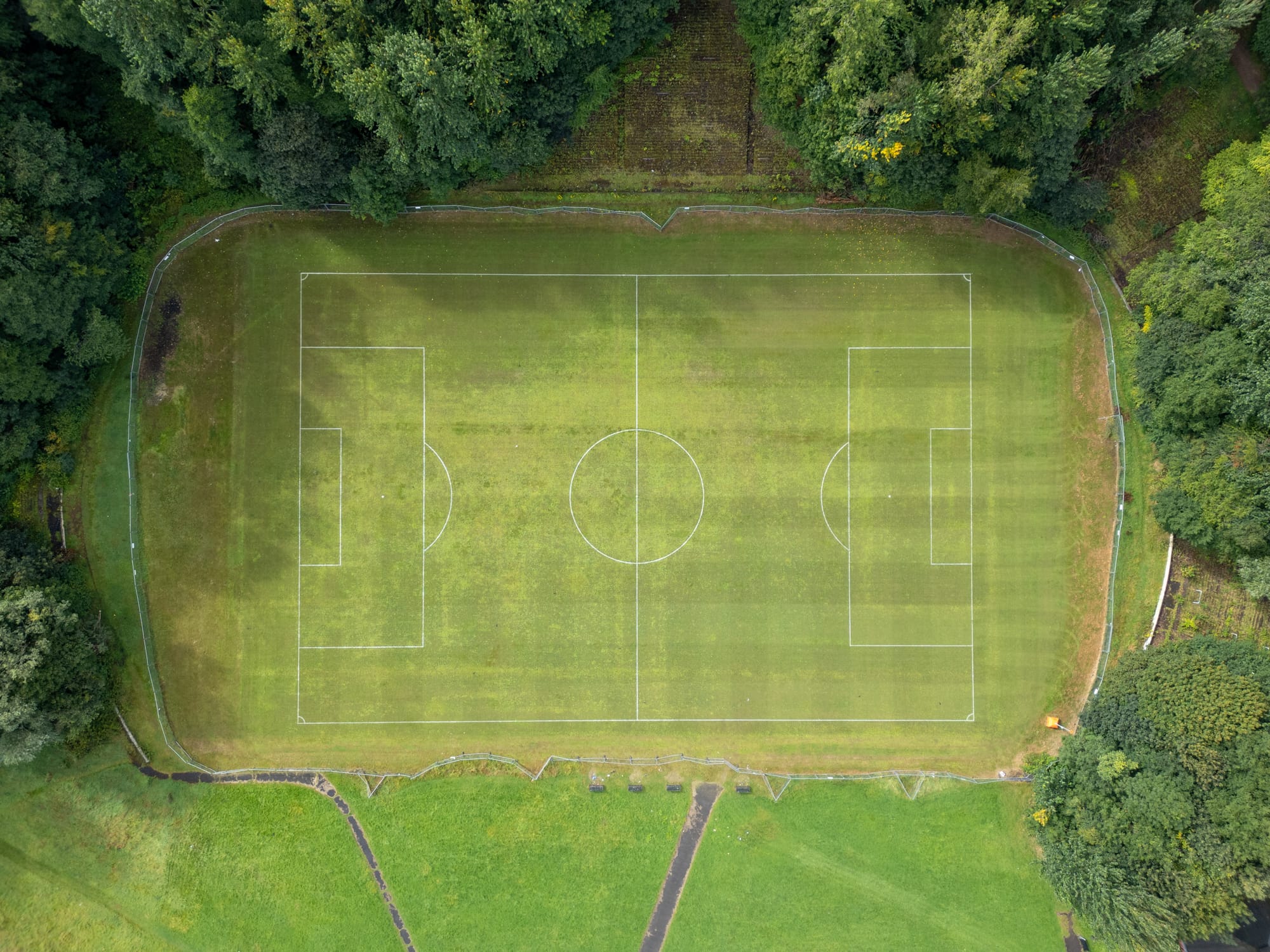 Aerial view of a grass football pitch surrounded by trees, seen from directly above