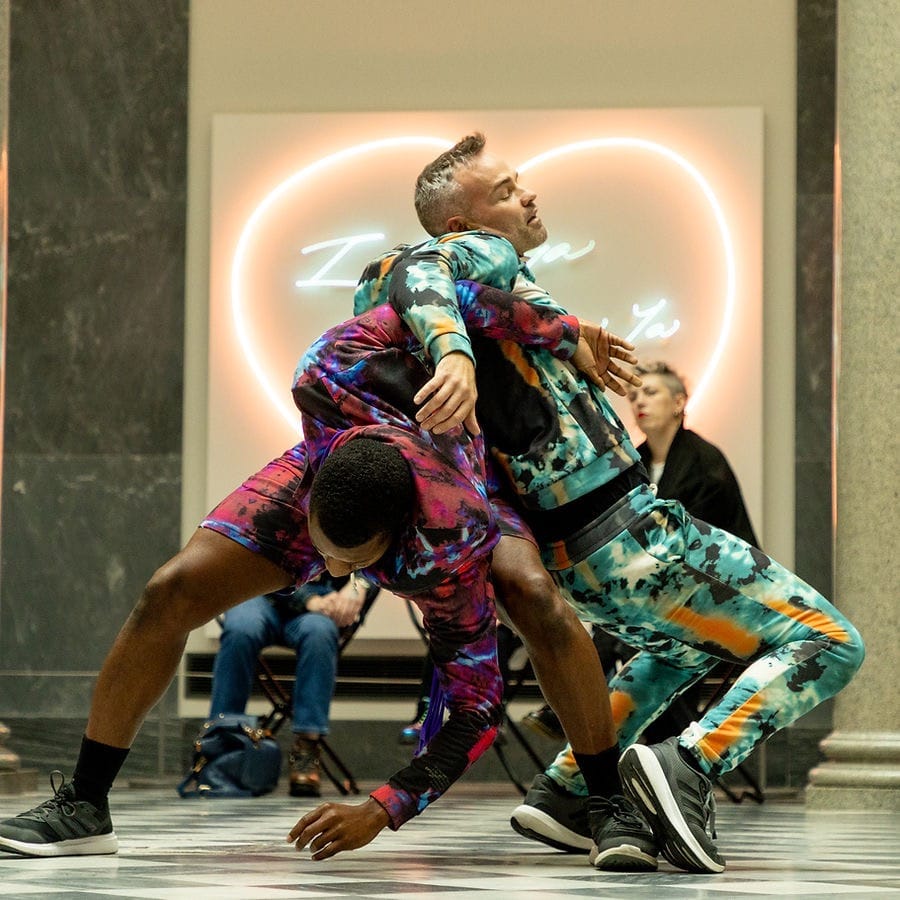 Two dancers in tie-dye costumes perform a lift at Aberdeen Art Gallery.