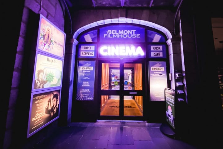 ight view of Belmont Filmhouse entrance lit with purple neon, showing posters and box office.