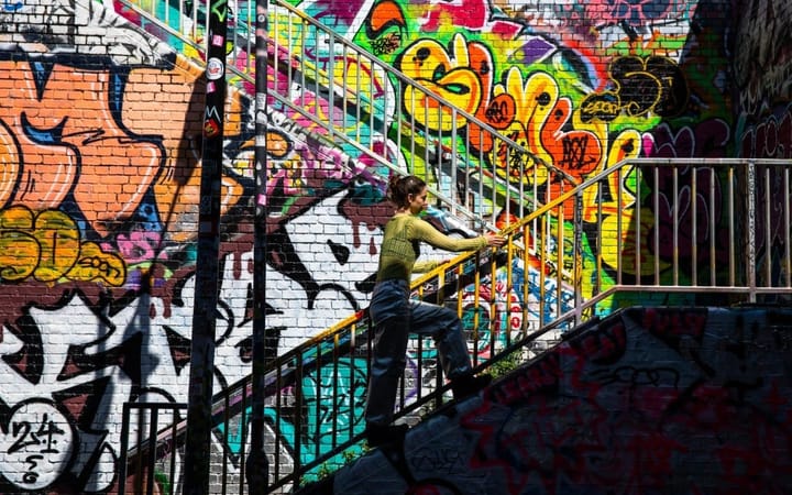 Alisa Oleva climbs stairs beside a brick wall covered in colourful graffiti. 