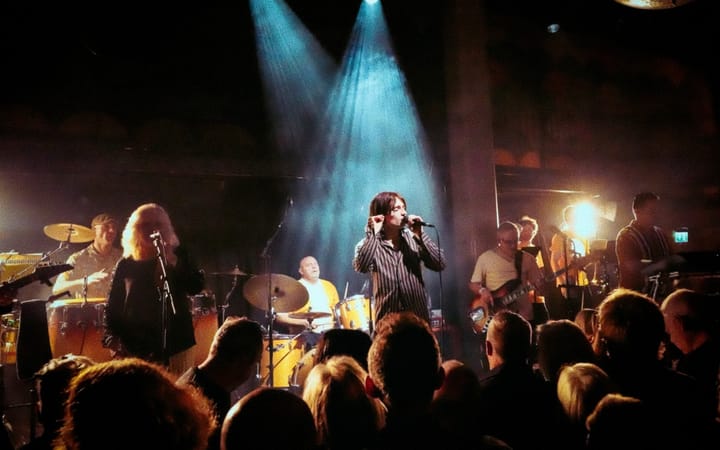 The Signatures perform live, vocalist in striped shirt at centre, crowd in foreground, blue stage lighting above