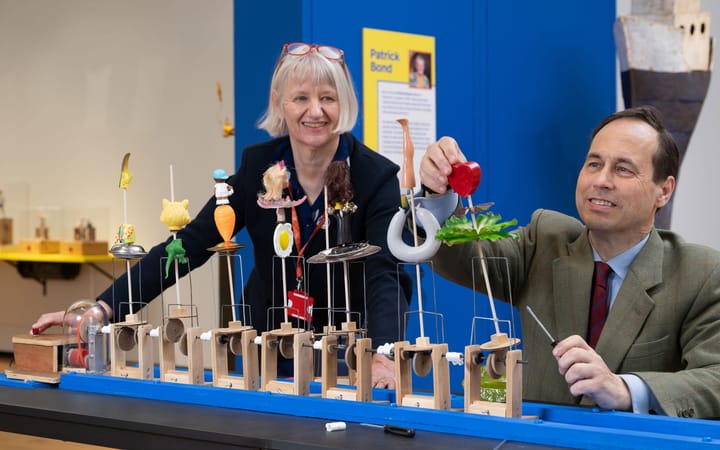 Two people operate a row of crank-driven automata at Aberdeen Art Gallery