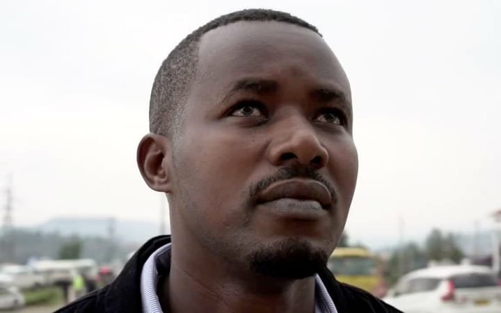 A man looks upward, photographed outdoors against a blurred urban background.