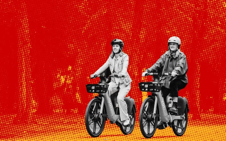 Two people riding Voi eBikes side by side, wearing helmets, against a red halftone background.