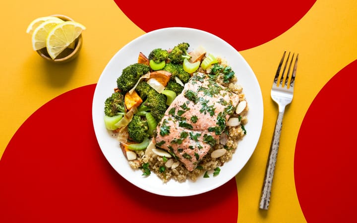 Herb-topped fish fillet with grains, roasted vegetables and lemon on a plate