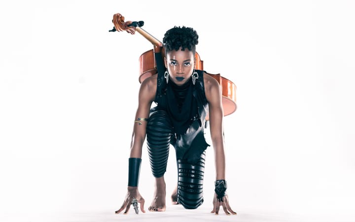 An athletic Ayanna Witter-Johnson on her knees like she was at the start of a race. She has her cello strapped to her back.