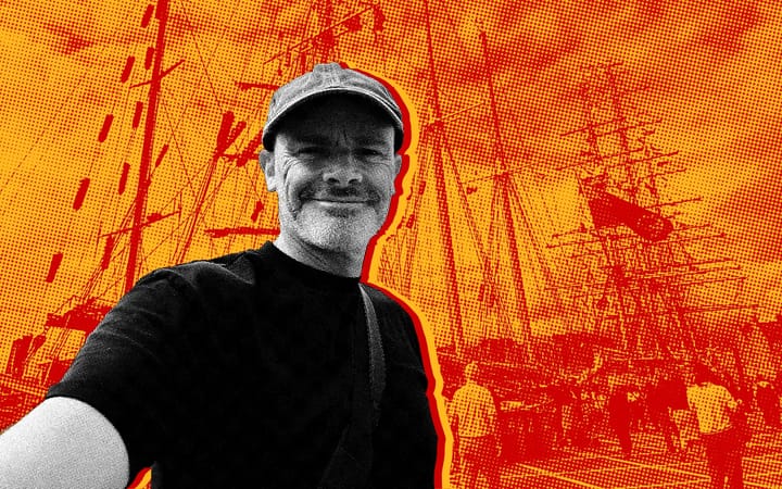 Clive Ramage in a flat cap, tall ship rigging behind him in orange and red